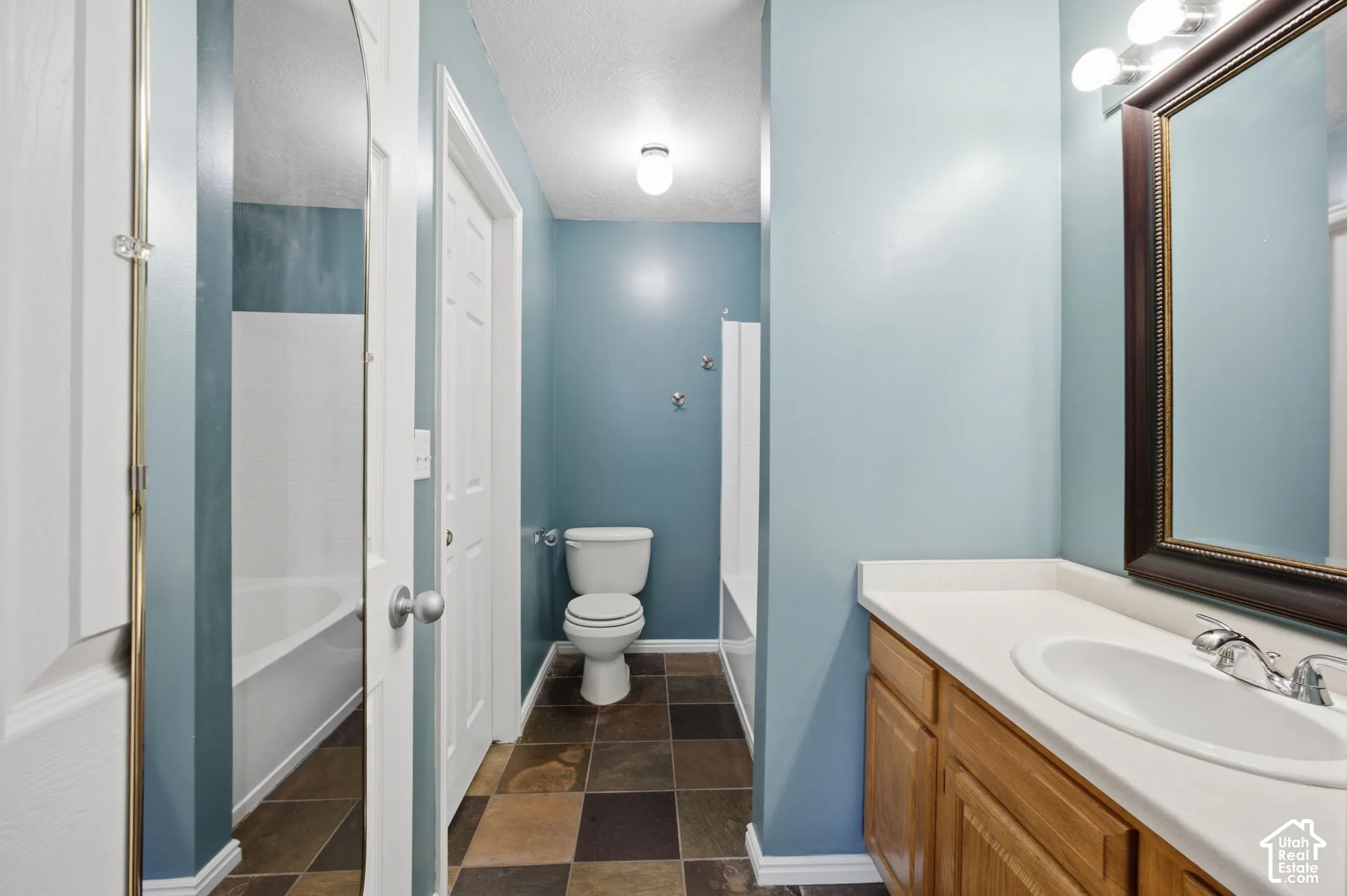 Bathroom featuring multicolor slate-style tile flooring, wood cabinetry with a white integrated sink, and an arched wall mirror