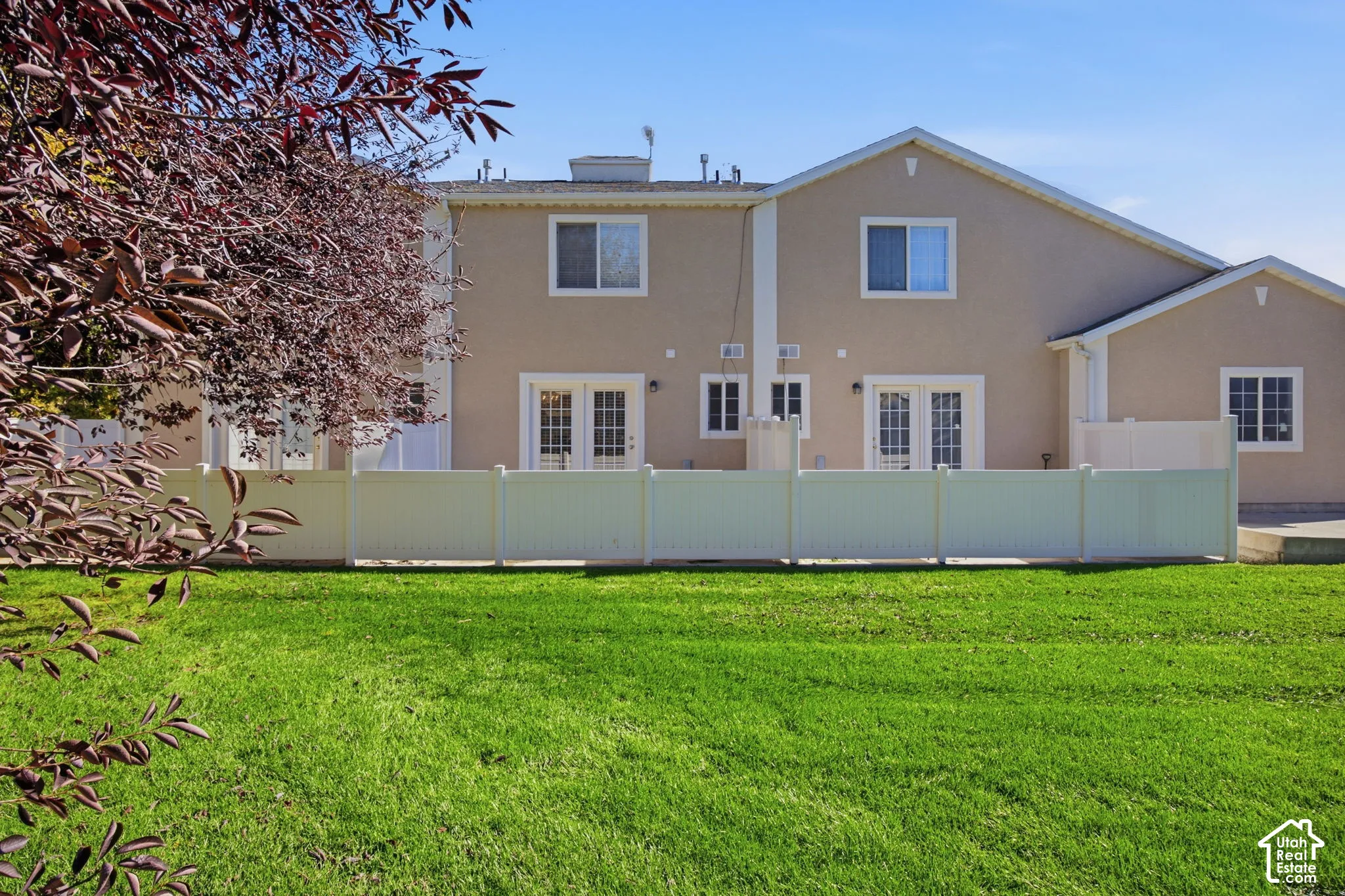 Stucco exterior featuring dual sets of French doors, a white vinyl privacy fence, and an expansive lawn