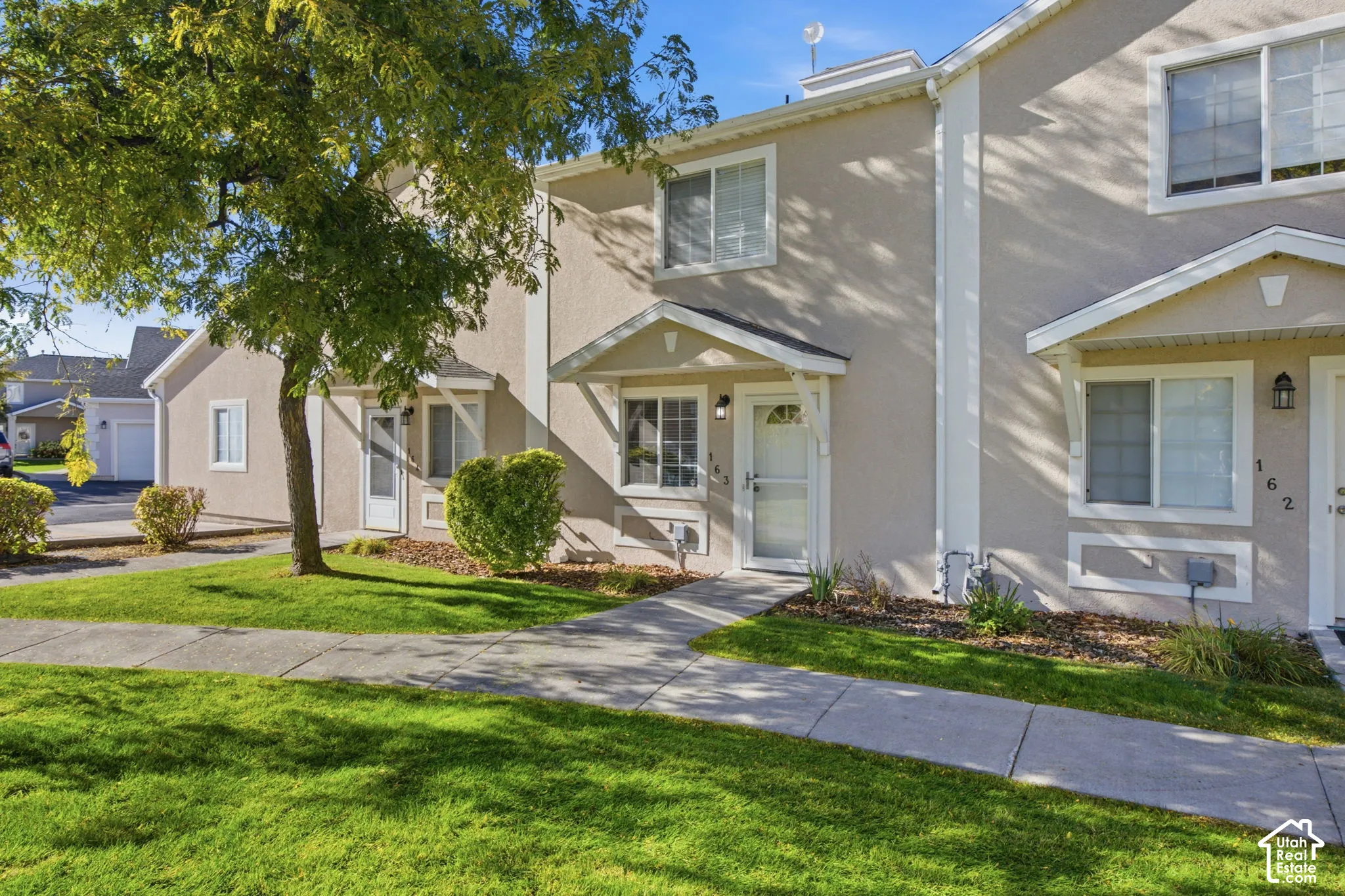 Stucco exterior featuring dual-pitched gabled entryways, concrete pedestrian walkways, and mature landscaping