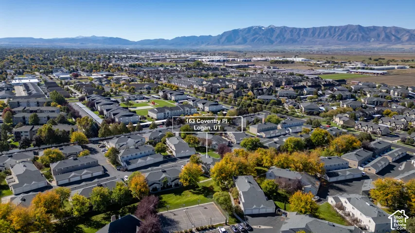 Aerial perspective of a multi-unit residential community featuring asphalt parking surfaces, mature deciduous trees, and a mountain range backdrop
