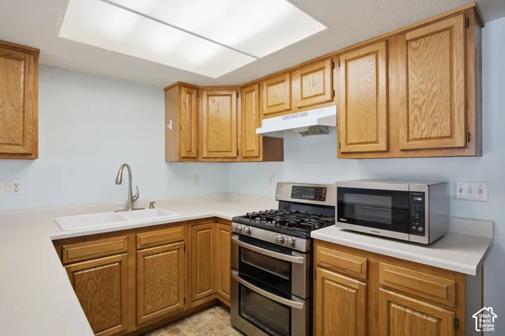 Kitchen featuring wood cabinetry, solid-surface countertops, dual-basin sink with high-arc faucet, and stainless steel gas range