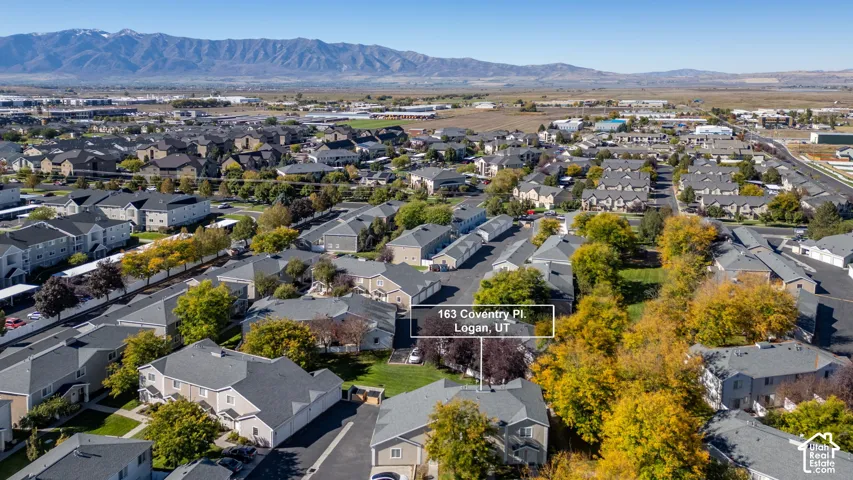 Aerial perspective of residential property featuring a composition shingle roof, asphalt-paved driveway, and surrounding mature trees with prominent mountain range backdrop