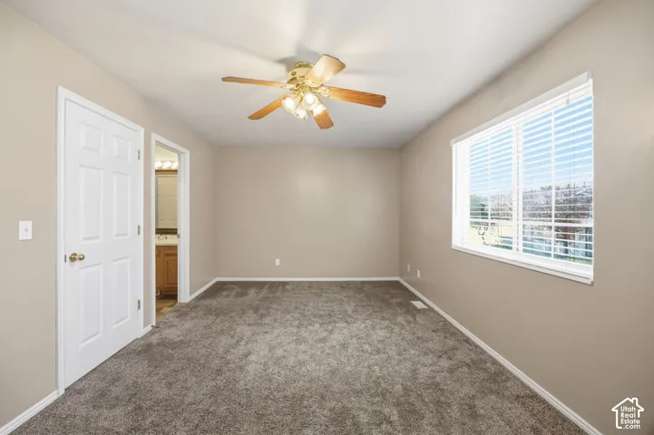 Neutral-toned interior featuring wall-to-wall carpeting, a multi-blade ceiling fan with integrated lighting, a multi-pane window with adjustable blinds, and a six-panel interior door