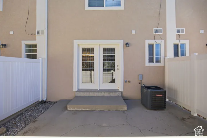 Exterior elevation featuring dual-lite French doors, a concrete patio, and white vinyl privacy fencing