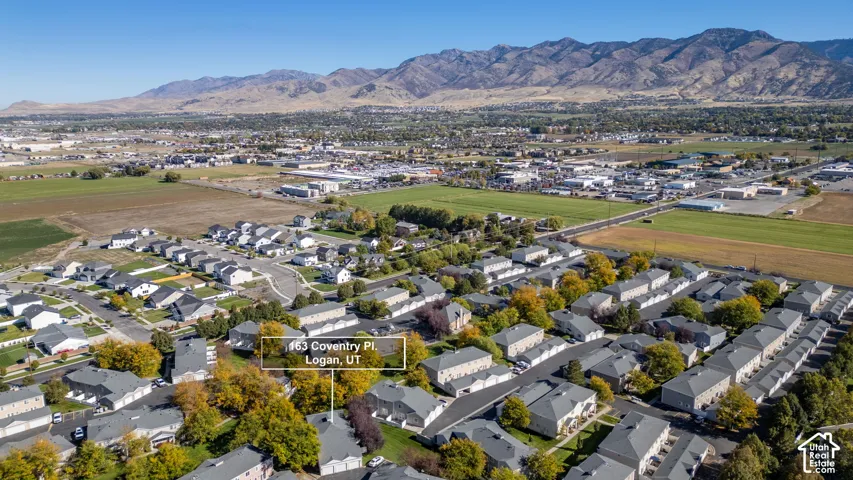 Aerial perspective of a multi-unit residential property featuring a gray shingled roof, attached garages, and a mountainous backdrop
