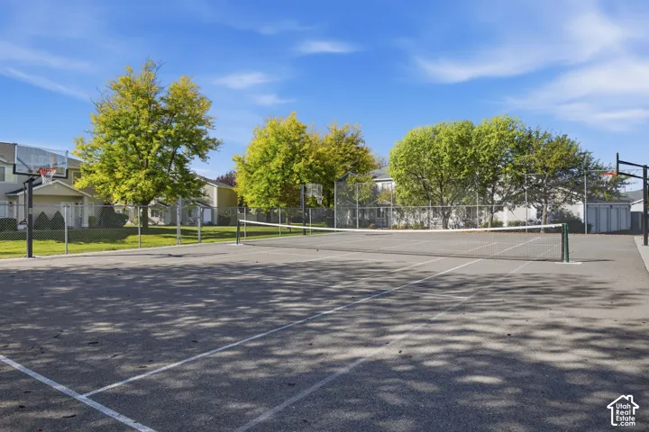 Multi-purpose paved court featuring a tennis net, basketball hoops, and perimeter fencing