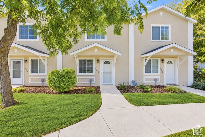 Two-story exterior featuring light-colored stucco siding, individual covered entryway gables, white trim details, and dual-pane windows