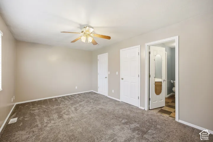 Neutral-toned room featuring plush wall-to-wall carpeting, a ceiling fan with integrated light fixture, two panel-style doors, and an entry to a tiled washroom with a decorative oval-inlay door