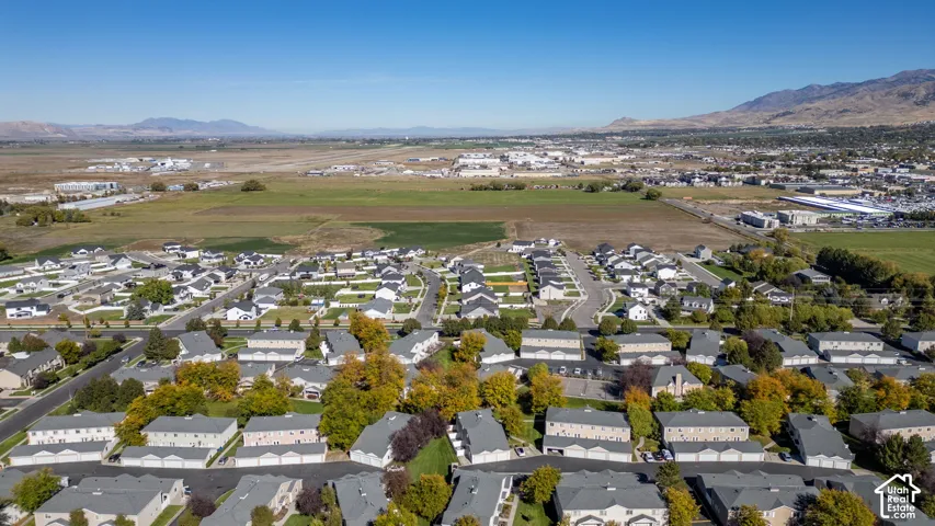 Aerial perspective of a multi-unit residential community featuring asphalt roadways, uniform roofing, mature deciduous trees, and surrounding mountain silhouettes