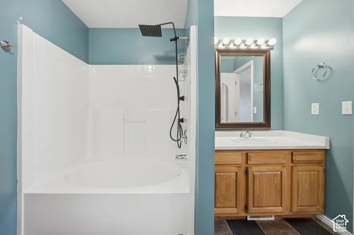 Bathroom featuring a deep soaking tub, white tile surround, matte black rainfall showerhead, wood-finish vanity with an integrated sink, and multi-bulb vanity lighting