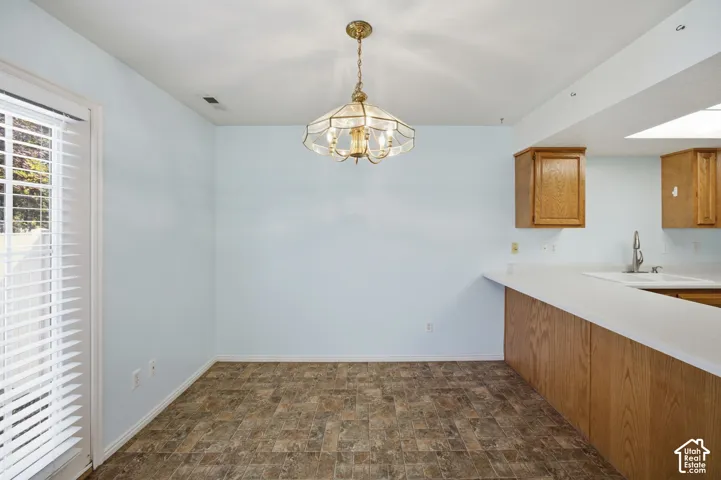 Dining area featuring tile flooring, a multi-arm brass pendant light fixture, wood-finish cabinetry, and a glass-paneled door with integrated blinds
