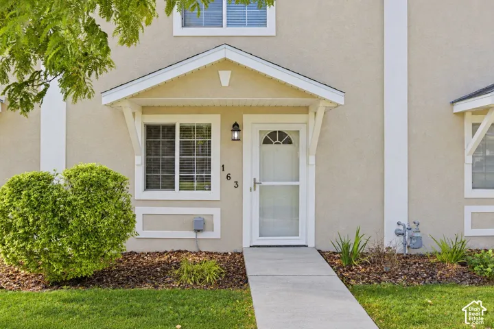 Stucco exterior featuring a gabled entryway, white-trimmed windows, a concrete walkway, and an arched-glass front door