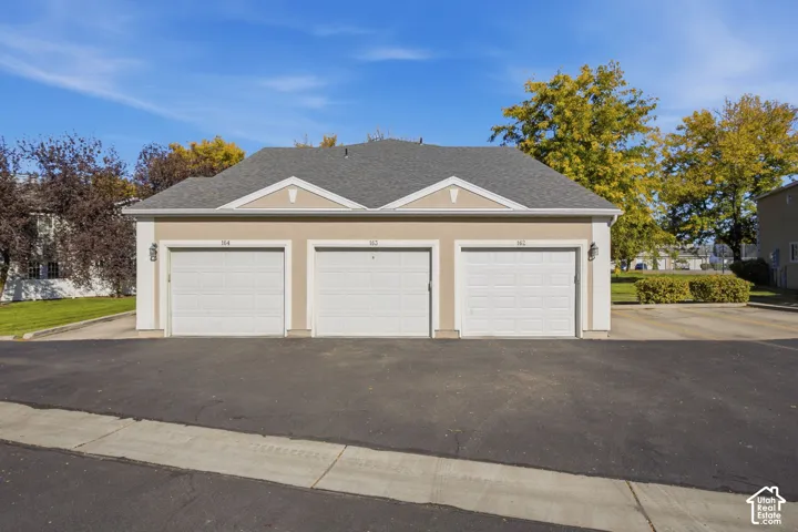 Detached three-car garage featuring a stucco exterior, asphalt shingle roofing, and three individual sectional garage doors
