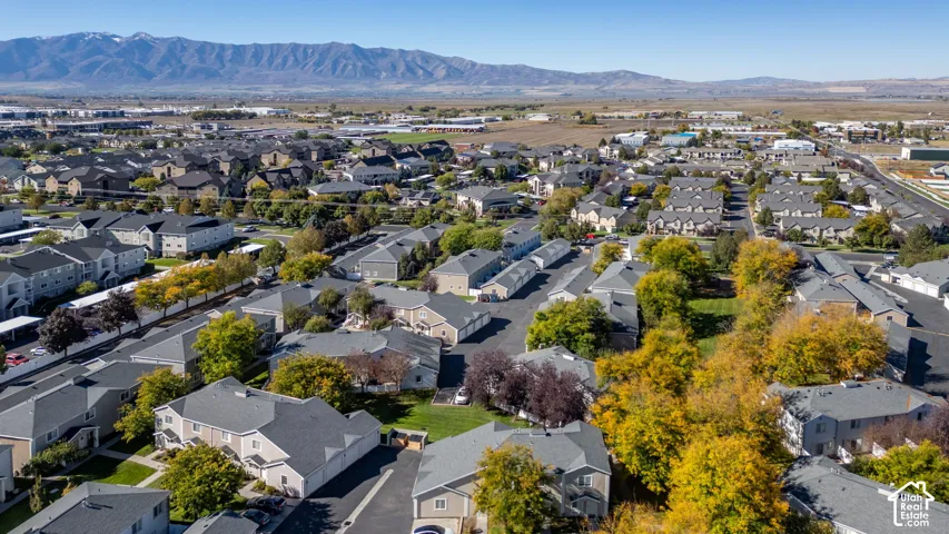 Aerial perspective featuring residential multi-unit structures, mature deciduous trees, asphalt driveways, and mountain range backdrop