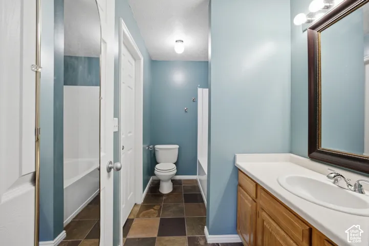 Bathroom featuring multicolor slate-style tile flooring, wood cabinetry with a white integrated sink, and an arched wall mirror