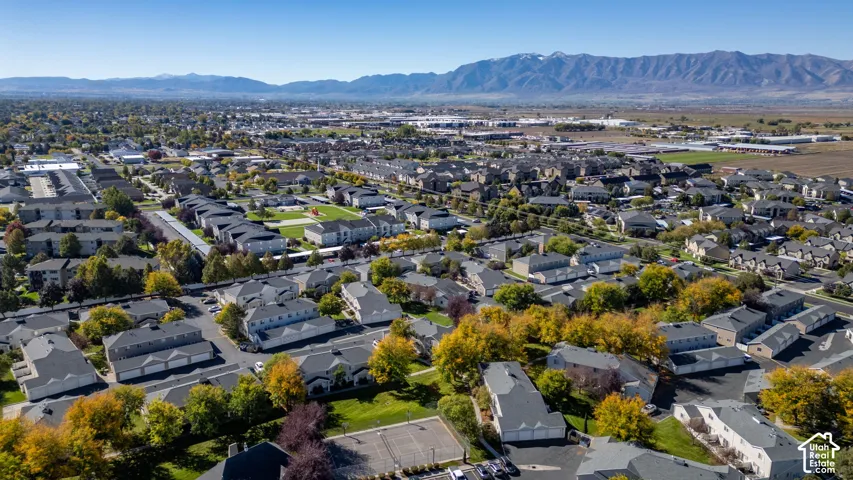 Aerial perspective of a multi-unit residential community featuring mature tree-lined streets, a paved tennis court, and prominent mountain range backdrop
