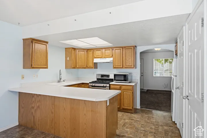 Kitchen featuring wood cabinetry, solid-surface countertops, peninsula seating, gas range, and recessed ceiling lighting