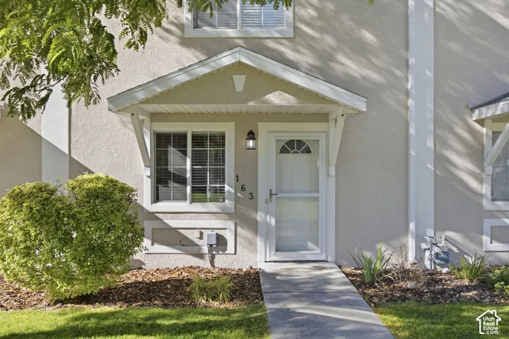 Stucco exterior featuring a covered entryway with gable roof detail, white-trimmed windows, glass-panel entry door, and exterior wall-mounted lighting