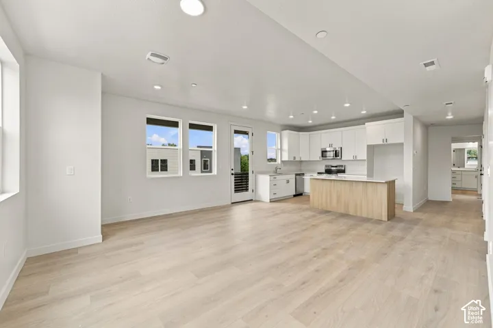 Open-concept kitchen and living area featuring wood-finish flooring, white cabinetry, a center island, recessed lighting, and large windows