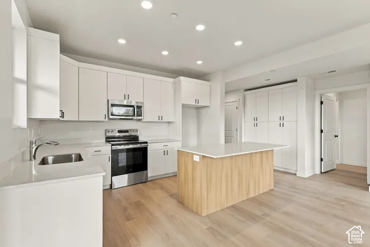 Kitchen featuring white shaker-style cabinetry, wood-finish center island, quartz countertops, stainless steel appliances, and recessed lighting
