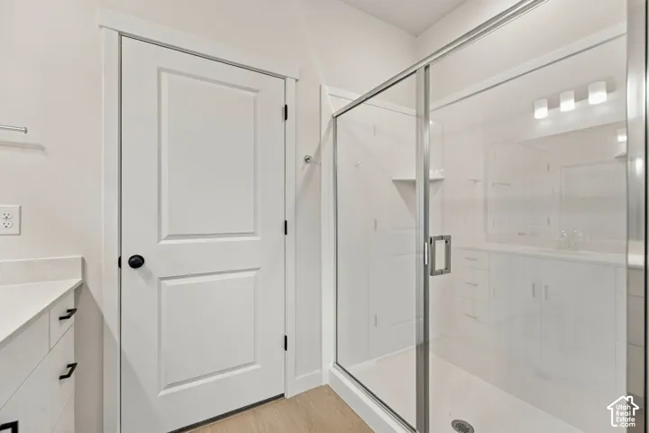 Bathroom featuring a walk-in shower with glass enclosure, vanity with stone-surface countertop, built-in cabinetry, and wood-finish flooring