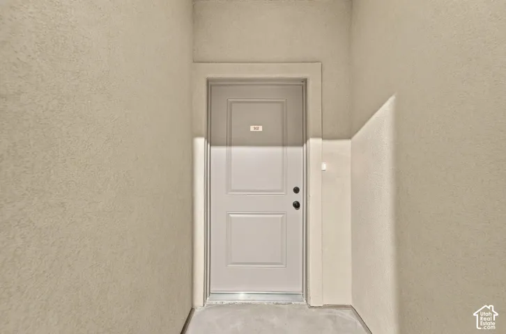 Entryway featuring a light-toned solid door with two rectangular panels, matte black hardware, and stucco-finished walls