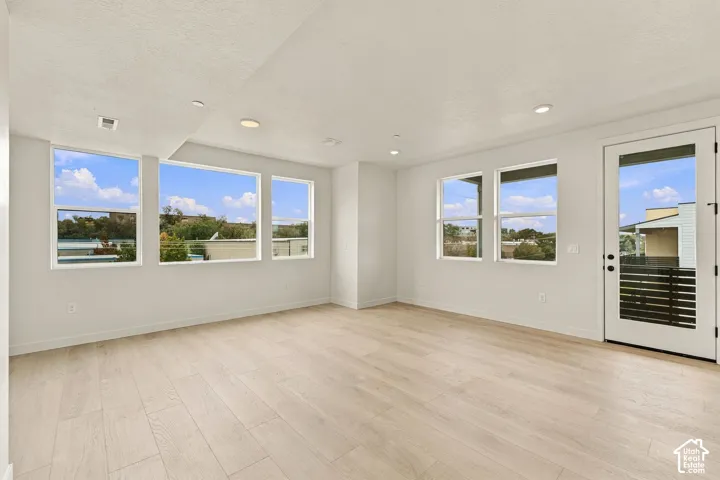 Open-concept room featuring wood-finish flooring, recessed lighting, multiple oversized windows, and a glass-paneled exterior door