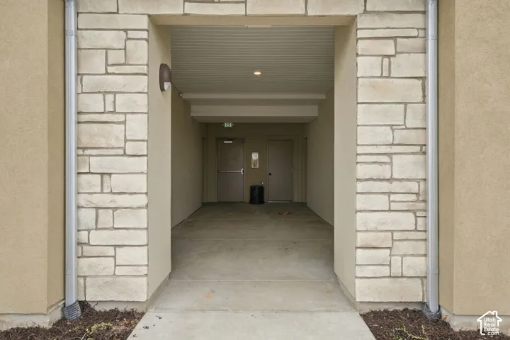 Exterior entryway featuring natural stone veneer cladding, stucco finish, concrete walkway, and recessed ceiling lighting