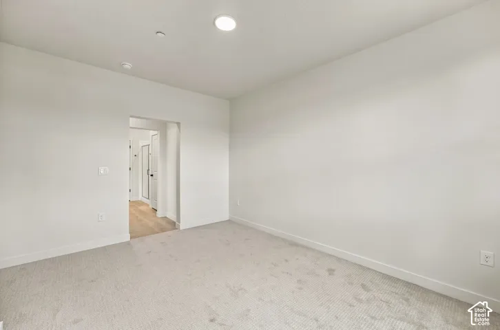 Neutral-toned interior room featuring wall-to-wall carpeting, recessed ceiling lighting, and a passage to an area with wood-finish flooring