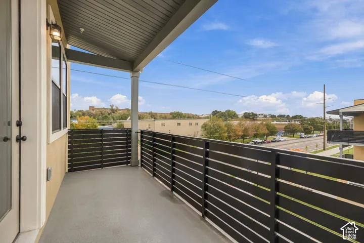 Covered balcony featuring horizontal slat metal railing, concrete flooring, exterior wall-mounted lighting, and a neutral stucco finish