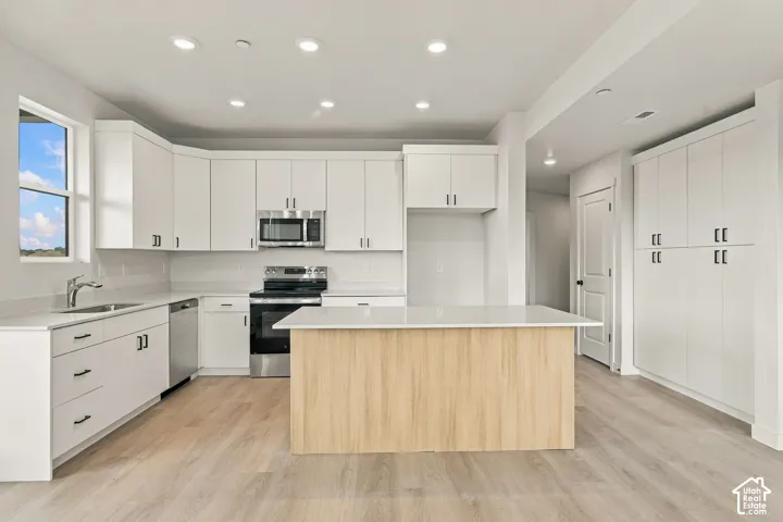 Kitchen featuring white shaker-style cabinetry, wood-finish center island, stone-surface countertops, stainless steel appliances, and recessed lighting