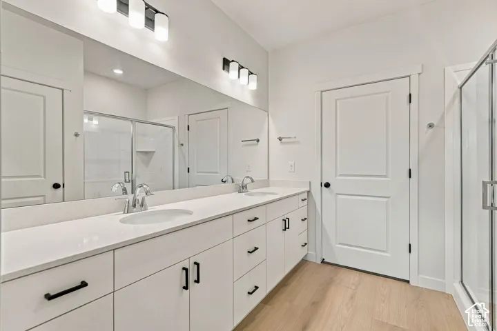 Dual-vanity cabinetry with matte black hardware, stone-surface countertop, full-width vanity mirror, dual-light vanity fixtures, and wood-finish flooring
