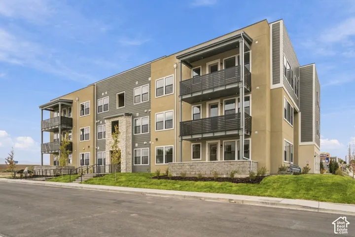 Multi-level exterior featuring a composite facade of earth-toned stucco and horizontal siding, stacked balconies with metal railings, stone veneer accents, and concrete hardscaping