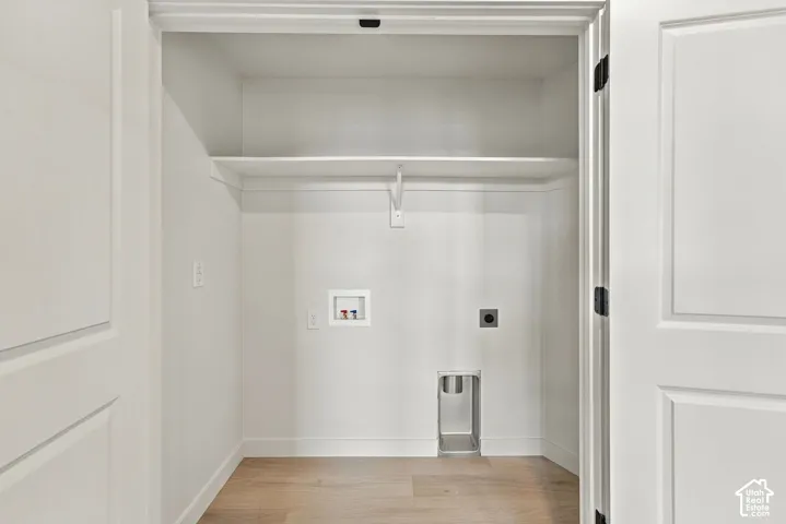 Utility closet featuring wood-finish flooring, dual-panel doors, overhead storage shelving, and dedicated washer and dryer hookups