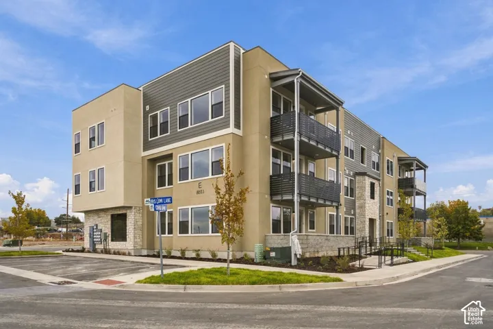 Multi-story exterior featuring a mix of stucco and horizontal siding, stacked metal balconies, stone veneer accents, and multi-pane windows