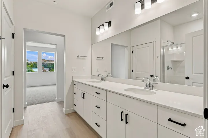 Double vanity with white cabinetry, matte black hardware, stone-surface countertops, dual integrated sinks, and triple-light vanity fixtures