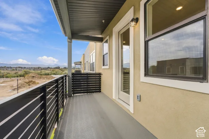 Covered balcony featuring horizontal metal railing, neutral-toned stucco exterior, and mountain backdrop