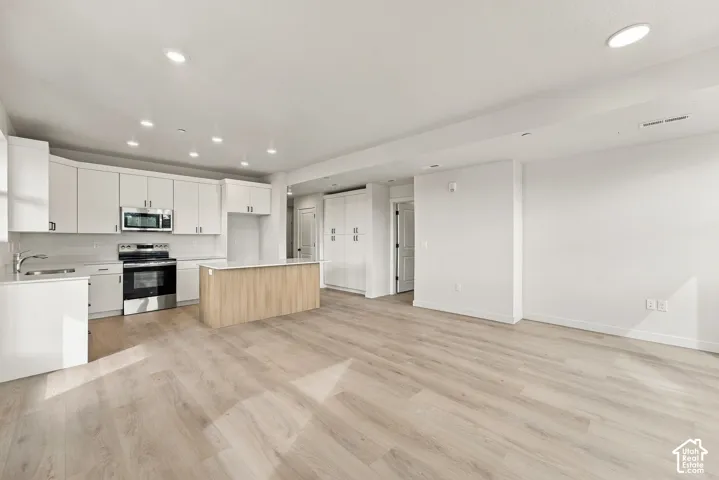 Kitchen featuring white shaker-style cabinetry, wood-finish center island, stainless steel appliances, recessed lighting, and wood-finish flooring