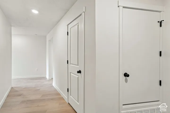 Interior hallway featuring wood-finish flooring, recessed lighting, and white paneled doors with matte black hardware