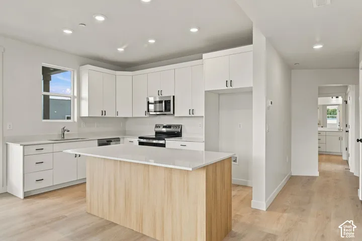 Kitchen featuring white shaker-style cabinetry, quartz countertops, a central island with wood-finish paneling, stainless steel appliances, and wood-finish flooring
