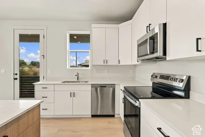 Kitchen featuring white shaker-style cabinetry, quartz countertops, stainless steel appliances, and wood-finish flooring