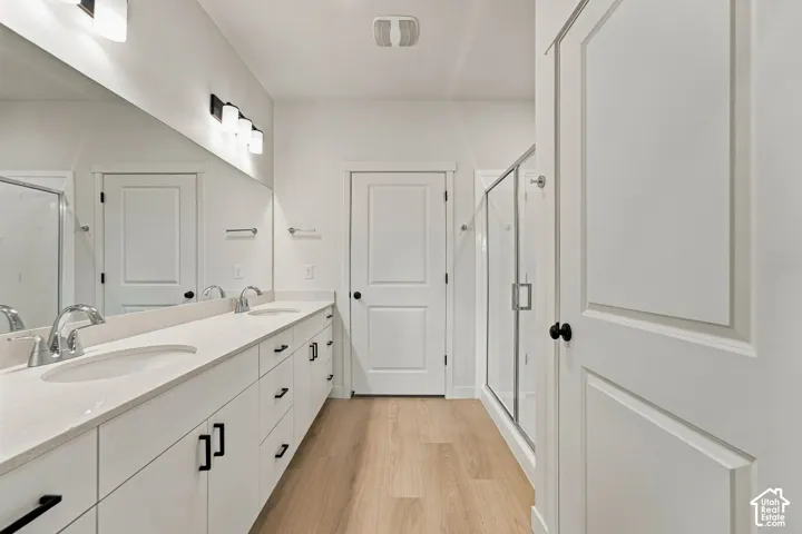 Double vanity with quartz countertops, undermount sinks, matte black hardware, glass-enclosed shower, and wood-finish flooring