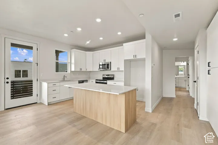 Kitchen featuring a central island with wood-finish cabinetry, white solid-surface countertops, recessed ceiling lighting, and stainless steel appliances
