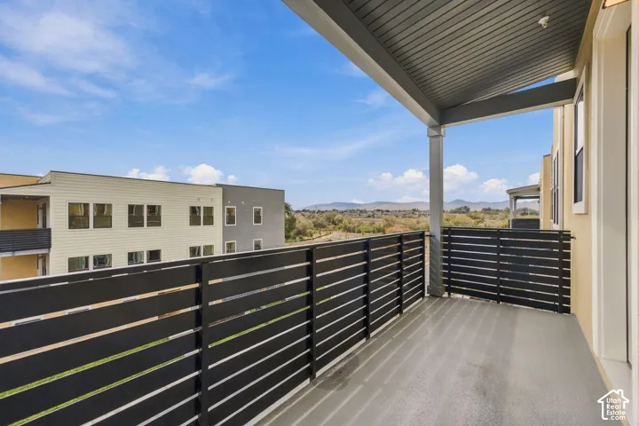 Covered balcony featuring horizontal black metal slat railings, a smooth finished floor, and a mountain backdrop