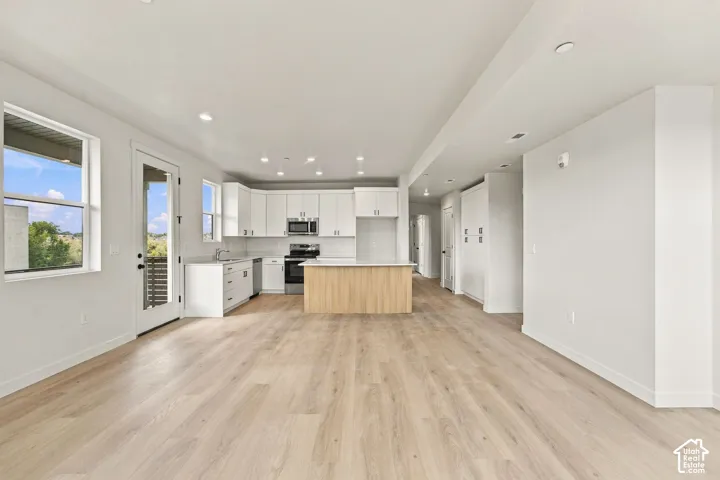 Open-concept kitchen featuring white shaker-style cabinetry, an island with wood-finish paneling, stainless steel appliances, recessed lighting, and wood-finish flooring