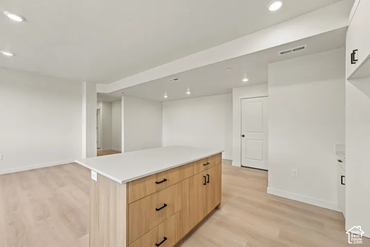 Kitchen island with a solid surface countertop, light wood-finish cabinetry, matte black hardware, recessed lighting, and wood-finish flooring