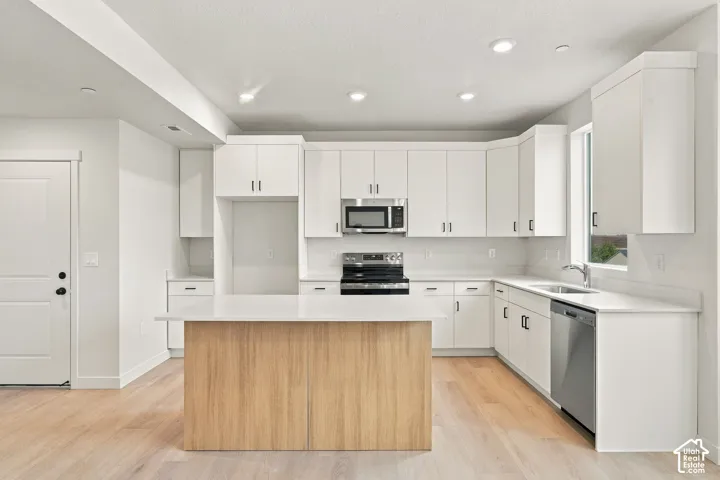 Kitchen featuring white cabinetry, wood-finish kitchen island, solid surface countertops, stainless steel appliances, and wood-finish flooring