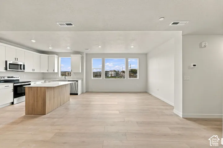 Open-concept kitchen featuring white shaker-style cabinetry, wood-finish kitchen island, stainless steel appliances, and wood-finish flooring throughout