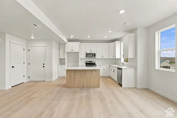 Kitchen featuring white cabinetry, wood-finish center island, light-toned wood-finish flooring, recessed lighting, and stainless steel appliances
