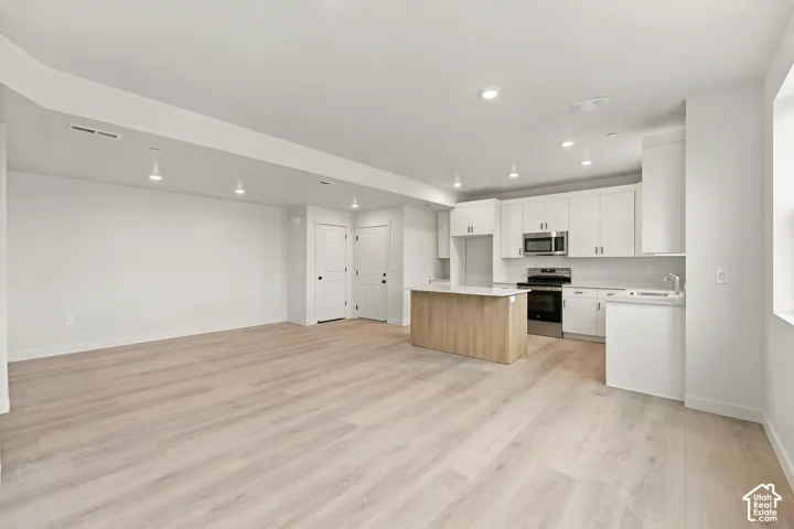 Open-concept kitchen and living area featuring wood-finish flooring, white shaker-style cabinetry, an island with a light-toned wood finish, stainless steel appliances, and recessed ceiling lighting